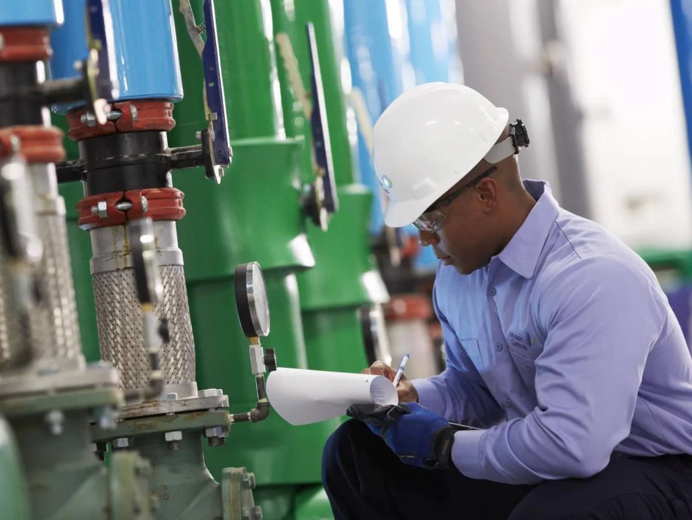 Mechanic recording equipment readings beside mechanical pipework